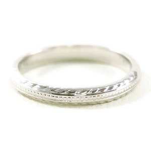 May include: A simple, silver wedding band with a delicate, engraved design.