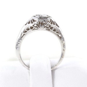 May include: A silver filigree engagement ring with a round, bezel-set diamond.