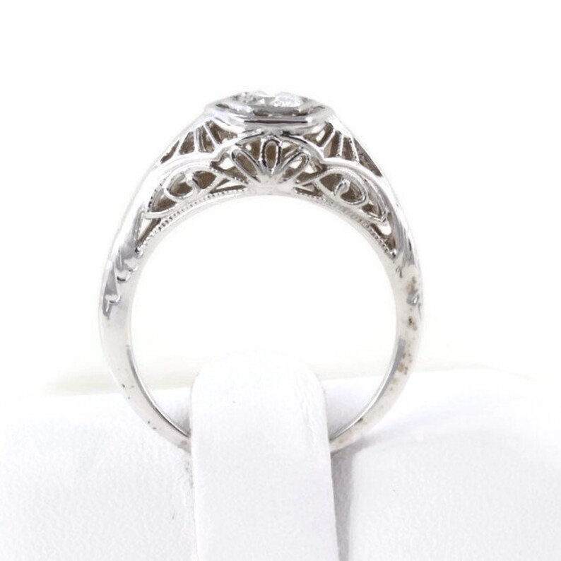 May include: A silver filigree engagement ring with a round, bezel-set diamond.