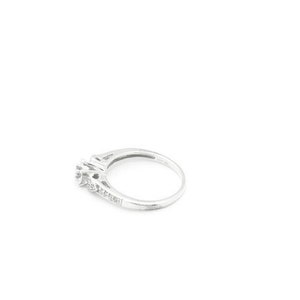 May include: A silver ring with a single large diamond and smaller diamonds set in the band.