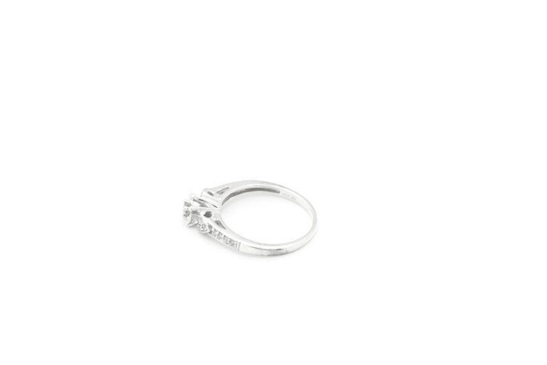 May include: A silver ring with a single large diamond and smaller diamonds set in the band.