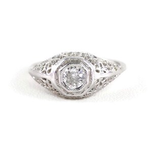 May include: A delicate silver ring with a filigree design and a single round diamond in the center.