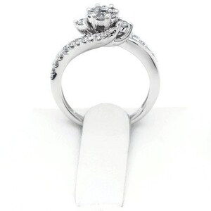 Op de afbeelding: Een zilveren ring met een cluster van kleine diamanten die in een bloemvorm zijn gezet. De band is gedraaid en bezet met kleinere diamanten.