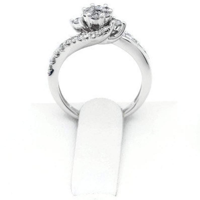 Op de afbeelding: Een zilveren ring met een cluster van kleine diamanten die in een bloemvorm zijn gezet. De band is gedraaid en bezet met kleinere diamanten.