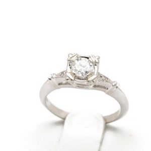 May include: A silver engagement ring with a round, clear diamond set in a delicate, ornate design.
