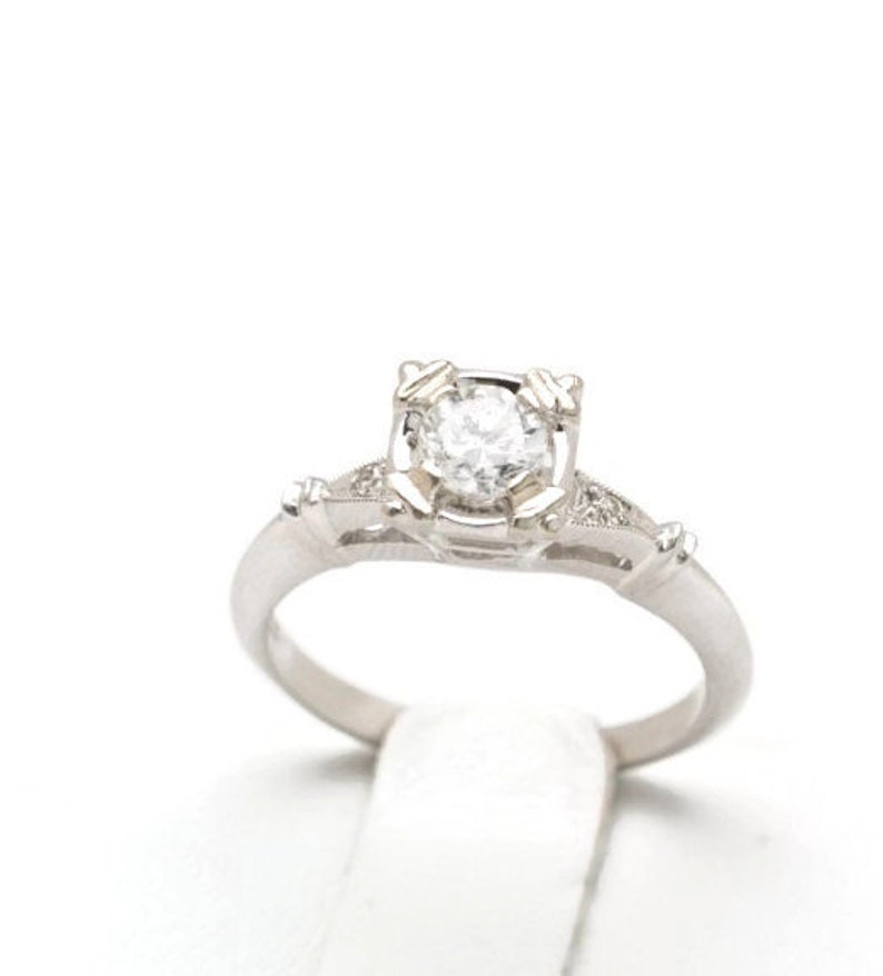 May include: A silver engagement ring with a round, clear diamond set in a delicate, ornate design.