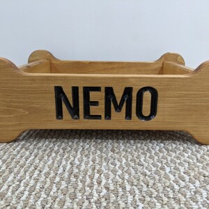 May include: A wooden dog bed shaped like a bone with the name "NEMO" carved into the front.