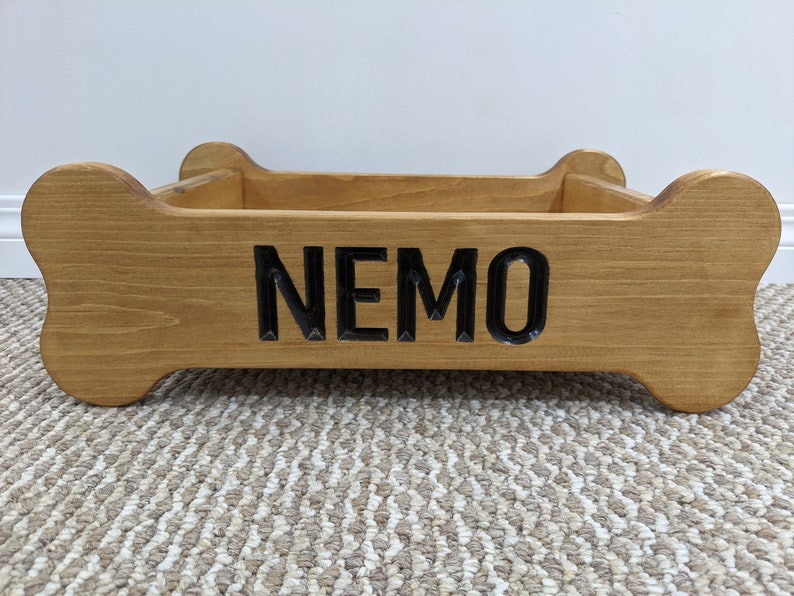 May include: A wooden dog bed shaped like a bone with the name "NEMO" carved into the front.