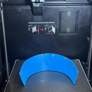 May include: A vibrant blue, curved plastic piece with multiple small, silver fixings. It sits on a black surface inside a 3D printer. The printer's print size is 270x270x256mm.