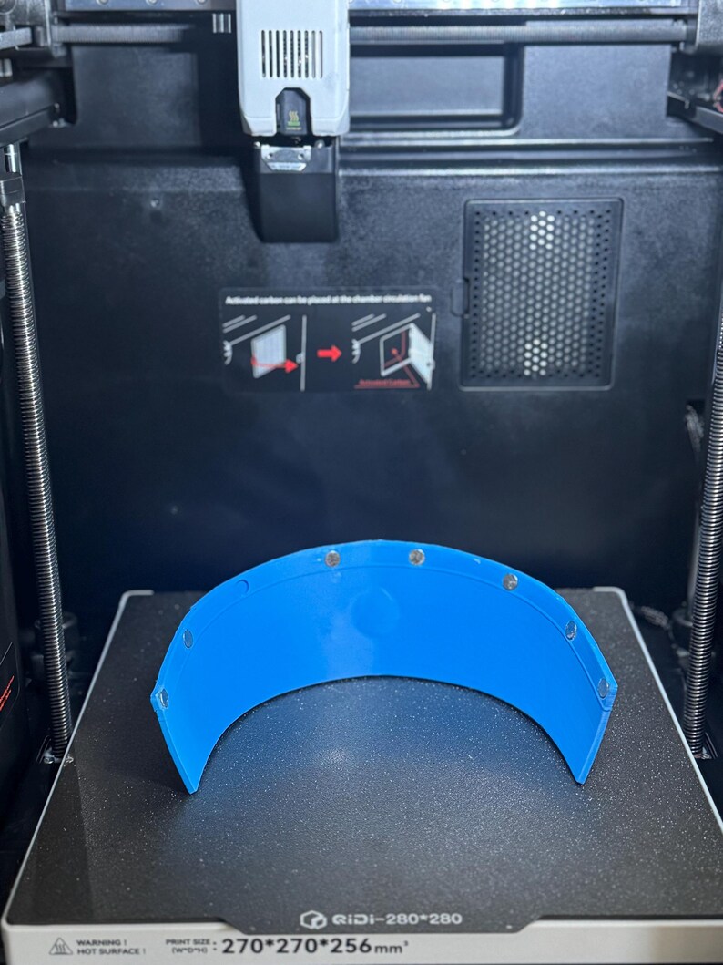 May include: A vibrant blue, curved plastic piece with multiple small, silver fixings. It sits on a black surface inside a 3D printer. The printer's print size is 270x270x256mm.
