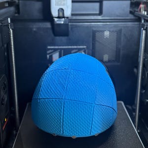 May include: A blue, textured, spherical object is being 3D printed. The object is divided into sections. The printer bed displays the text "RIDI-280*280" and "PRINT SIZE: 270*270*256mm&sup3;". The printer is enclosed in a black frame.