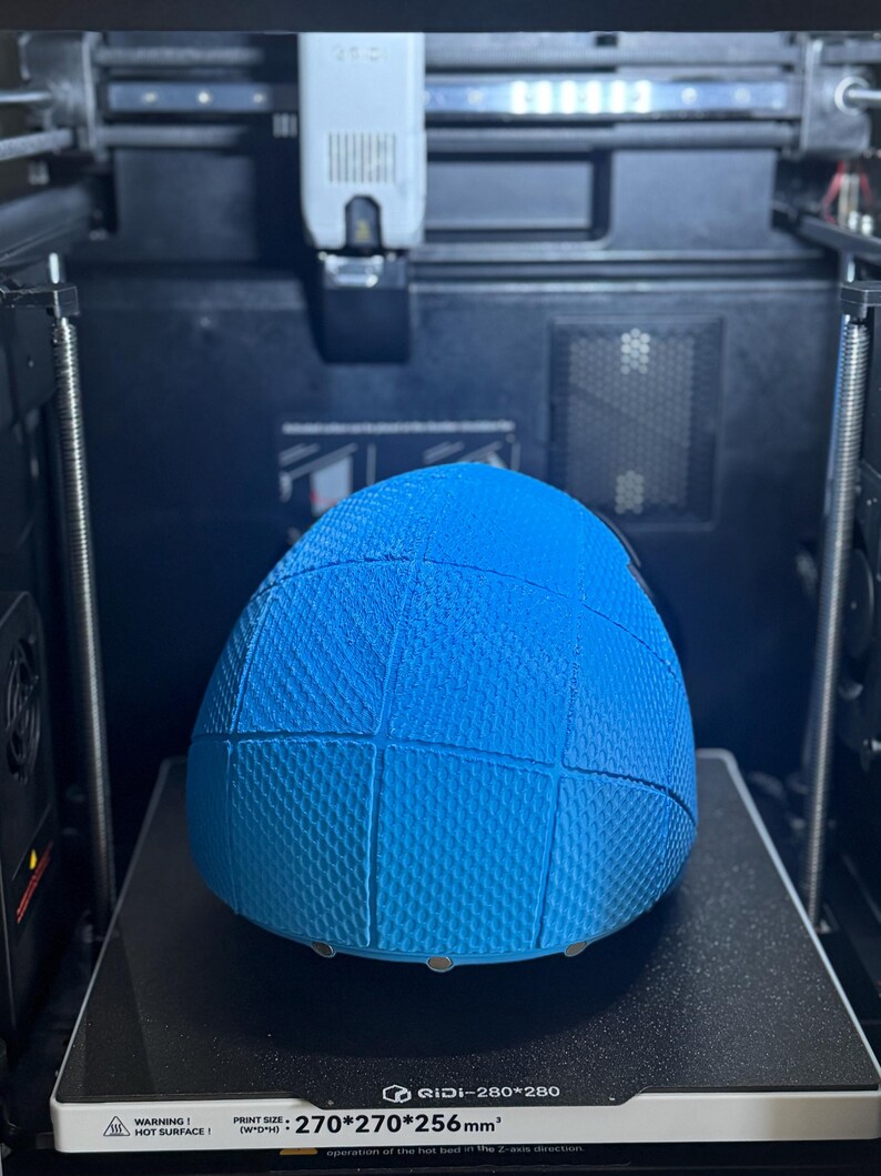 May include: A blue, textured, spherical object is being 3D printed. The object is divided into sections. The printer bed displays the text "RIDI-280*280" and "PRINT SIZE: 270*270*256mm&sup3;". The printer is enclosed in a black frame.