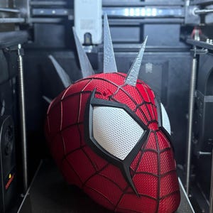 May include: A red and black Spider-Man mask with white eye lenses is being 3D printed. The mask has a webbed pattern and is in the process of being created inside a 3D printer. The printer bed has the text "GIDI-280*280" and "270*270*256mm&sup2;".