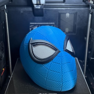 May include: A blue Spider-Man helmet with black eye frames and a textured surface, 3D printed on a black platform. The print bed size is 270x270x256mm. The helmet is in a 3D printer.
