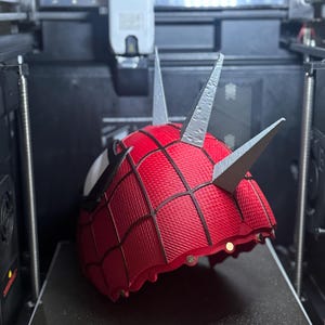 May include: A red and black Spider-Man mask with silver spikes is being 3D printed. The mask has a textured pattern and white eye details. The printer bed has the text "GIDI-280*280" and "270*270*256mm&sup3;".