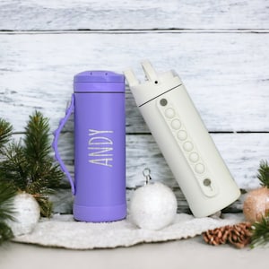 May include: Two insulated water bottles. One is lavender with the name "ANDY" etched on the side. The other is white with a pop-it style grip. The bottles are on a white surface with Christmas decorations.