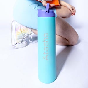 May include: A turquoise water bottle with a purple lid and a silver inscription that reads "Akasha".