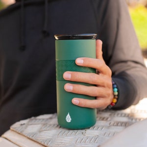 May include: A green reusable travel mug with a black lid and a white leaf logo. The mug has a textured band around the middle.