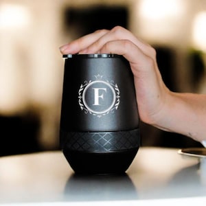 May include: A black stainless steel tumbler with a diamond pattern on the bottom. The tumbler has a white monogram with the letter "F" in a decorative circle.