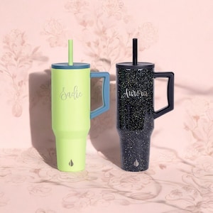 May include: Two stainless steel travel mugs with lids and handles. The mug on the left is light green with the name "Sadie" engraved on it. The mug on the right is black with a glittery finish and the name "Aurora" engraved on it.