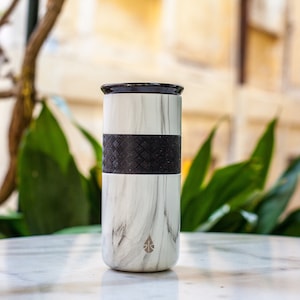 May include: A white marble travel mug with a black rubber band around the middle. The mug has a black lid and a small water drop logo on the front.
