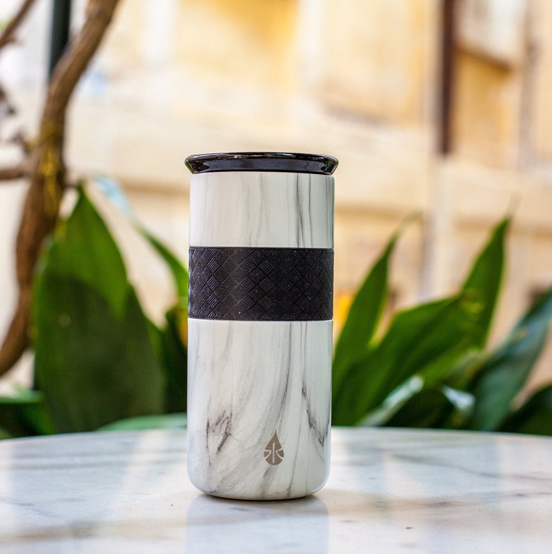 May include: A white marble travel mug with a black rubber band around the middle. The mug has a black lid and a small water drop logo on the front.