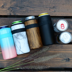 May include: Four insulated can coolers in different colors and patterns: blue and pink ombre, white marble, brown wood grain, and black. Two empty aluminum cans are also shown.