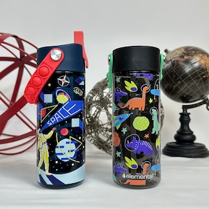 Peut inclure: Deux bouteilles d'eau r&eacute;utilisables avec des motifs color&eacute;s. Une bouteille pr&eacute;sente un th&egrave;me spatial avec un astronaute et des plan&egrave;tes. L'autre bouteille pr&eacute;sente un th&egrave;me dinosaure avec des dinosaures color&eacute;s. Les deux bouteilles ont un fond noir et sont en plastique transparent.