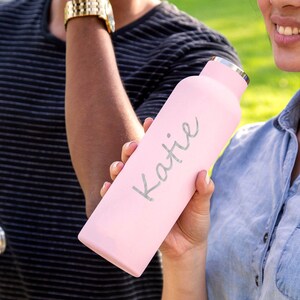 May include: A pink stainless steel water bottle with a silver lid and the name "Katie" written in silver lettering.