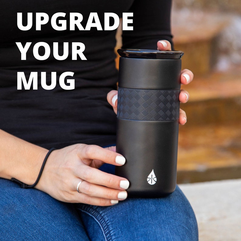 May include: A black travel mug with a textured black band around the middle. The mug has a white logo of a water drop on the bottom. The text "Upgrade Your Mug" is in white letters on a black background.
