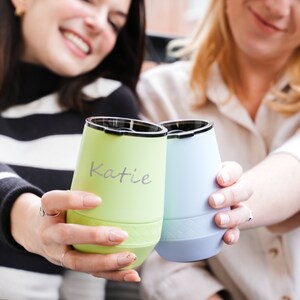 Puede incluir: Dos amigas brindando con vasos de vino aislados de color verde y azul. El vaso verde tiene el nombre "Katie" escrito en &eacute;l.
