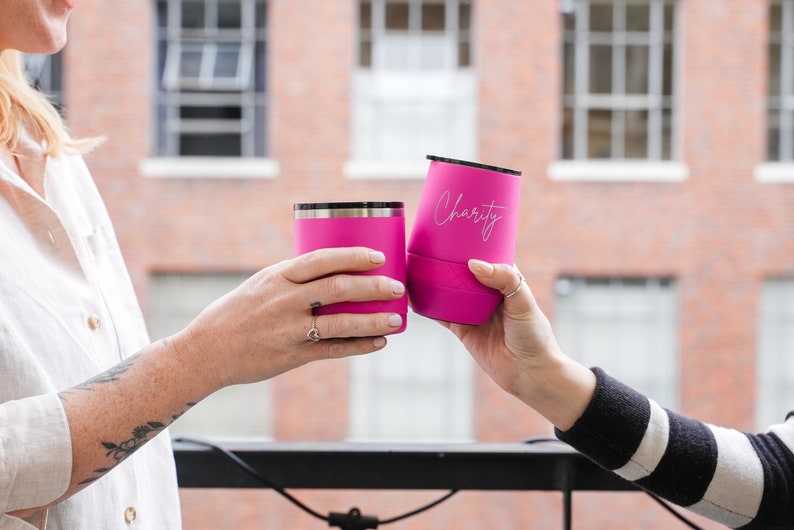 Puede incluir: Dos vasos de acero inoxidable de color rosa con tapas. El vaso de la derecha tiene la palabra "Charity" grabada.