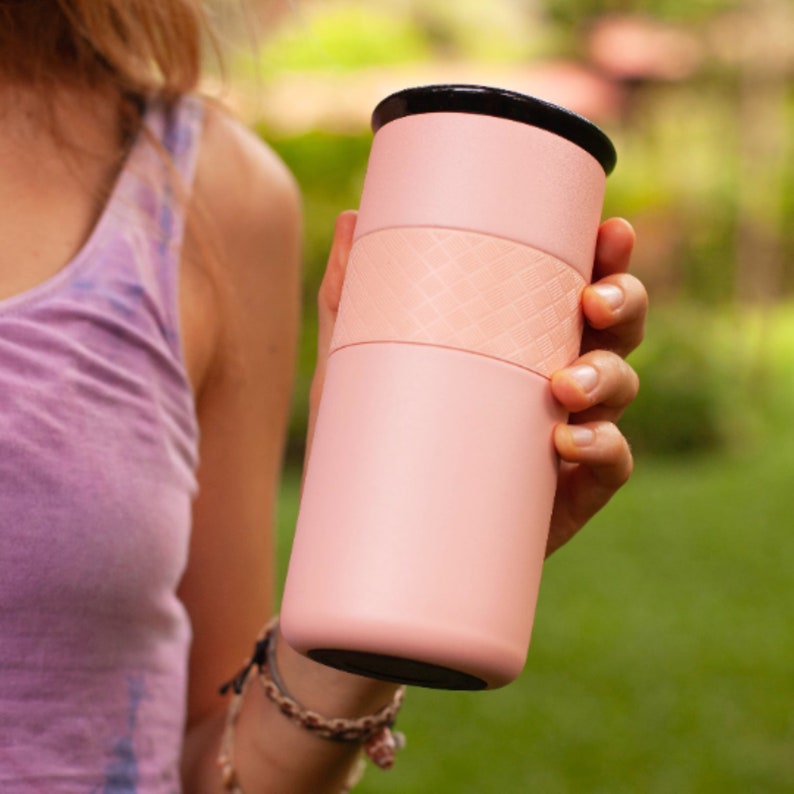 May include: A pink travel mug with a black lid and a textured band around the middle.