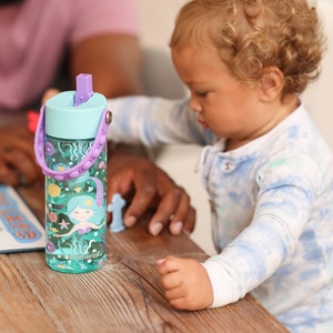 Peut inclure: Une bouteille d'eau bleue et violette avec un motif de sir&egrave;ne et un couvercle pop-up. La bouteille a une poign&eacute;e en silicone textur&eacute;e avec des bosses violettes.