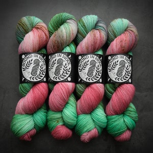 May include: Four skeins of yarn in shades of pink, green, and brown. The yarn is wrapped around itself and tied with a black label that says "Bound in Wool".
