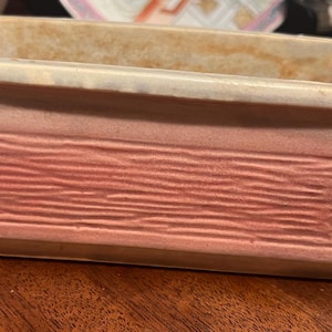 May include: A rectangular ceramic planter with a light brown top, a white middle section, and a pink bottom with a textured, horizontal stripe pattern.