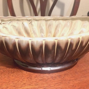 May include: An oval ceramic bowl featuring a scalloped, fluted exterior design. The piece displays a two-tone color scheme with a creamy off-white interior and upper rim that transitions into a deep, dark brown glaze toward the base.