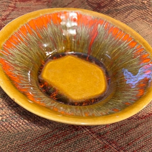 May include: A brown ceramic bowl with a glazed finish. The bowl has a unique design with orange, green, and blue streaks. The bowl is perfect for serving snacks or desserts.