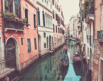 May include: A gondola with a gondolier in a red shirt is floating down a narrow canal in Venice, Italy. The canal is lined with colorful buildings with balconies and windows.