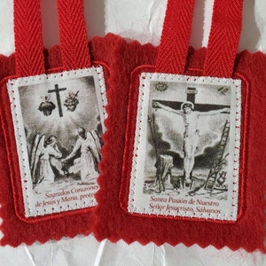 May include: Two red felt prayer cards with white stitching around the edges. The left card features a black and white image of two angels with a cross and two hearts above them. The text below the image reads "Sagrados Corazones de Jesus y Maria, prote". The right card features a black and white image of Jesus on the cross. The text below the image reads "Santa Pasión de Nuestro Señor Jesucristo, Sálvanos".