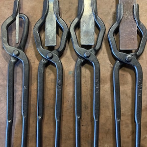 May include: Four black metal tongs with different sized flat metal pieces in the jaws. The tongs are labeled with the numbers "16", "1/1", "1/1/4", and "1/1/2".