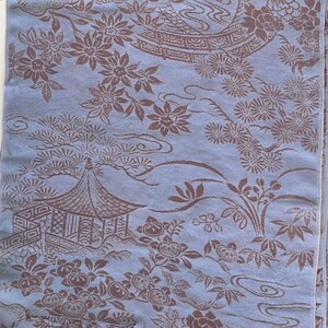 May include: A light blue fabric with a repeating pattern of brown floral and architectural designs. The pattern includes flowers, trees, and a pagoda-style building, creating an Asian-inspired aesthetic.