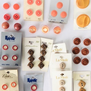 Puede incluir: Una colección de botones vintage en varias formas, tamaños y colores, incluyendo coral, marrón y beige. Algunos botones aún están en sus tarjetas originales, con marcas como "Elan Buttons" y "Majestic Buttons".