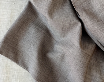 Puede incluir: Primer plano de una tela doblada con un tejido texturizado. La tela es de color marrón apagado, con sutiles variaciones de tono. Los pliegues crean sombras y profundidad, resaltando la textura y la caída del material. La tela parece ser de peso medio, adecuada para ropa o decoración del hogar.