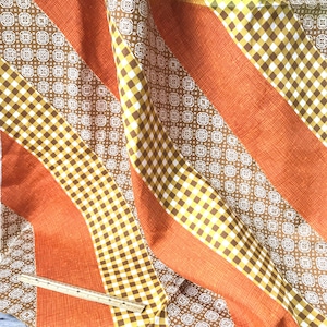 May include: Orange and brown fabric with a checkered and geometric pattern. The fabric is folded and draped.