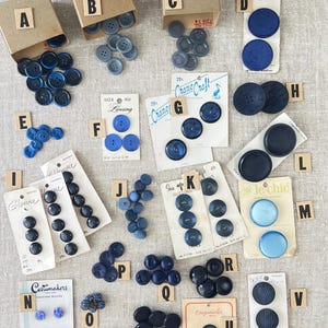 May include: Assortment of vintage buttons in various colors, including blue, black, and white. The buttons are displayed on cards with different brand names, such as "Crane Craft", "Lansing", and "Glamour".