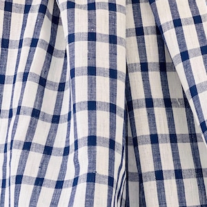 Puede incluir: Primer plano de una tela de cuadros blancos y azules. La tela tiene un patrón de cuadros clásico con cuadrados alternos de blanco y azul marino. La tela está doblada, creando sombras suaves y textura.