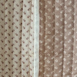 以下が含まれることがあります： 花柄の2つの布パネルのクローズアップ。1つのパネルはオフホワイトに茶色の花のアクセント、もう1つは茶色にオフホワイトの花のアクセント。白いストリップがパネルを分けています。