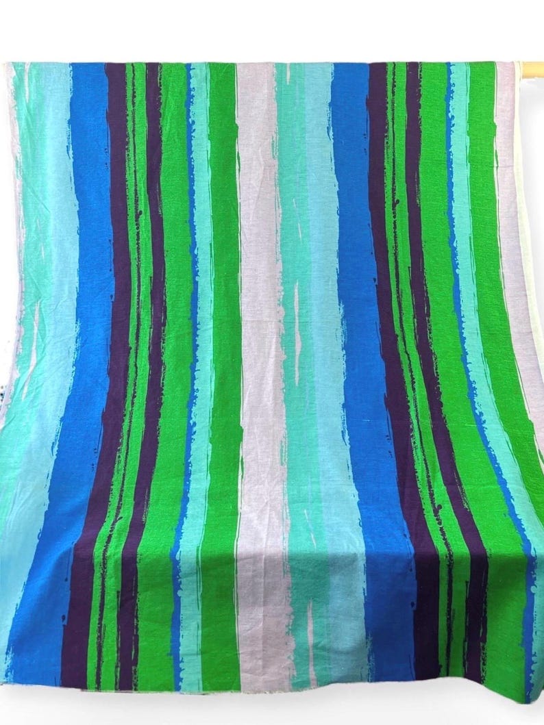 May include: A fabric with a striped pattern in shades of blue, green, and purple. The stripes are painted on a white background.