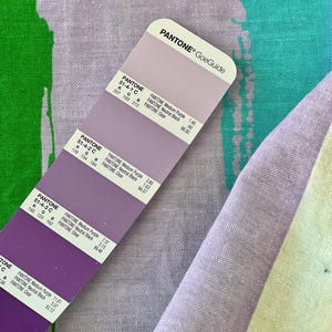 May include: A color swatch card with different shades of purple. The card is labeled "PANTONE&reg; GoeGuide" and includes the Pantone color numbers and names for each shade.